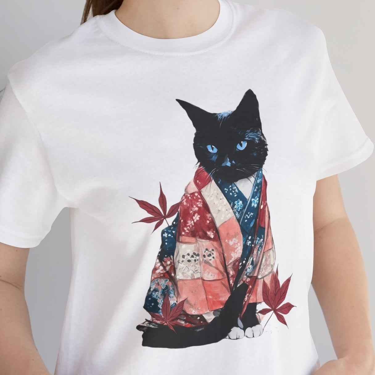 Person wearing a white t-shirt with a black cat design, standing indoors next to a plant.