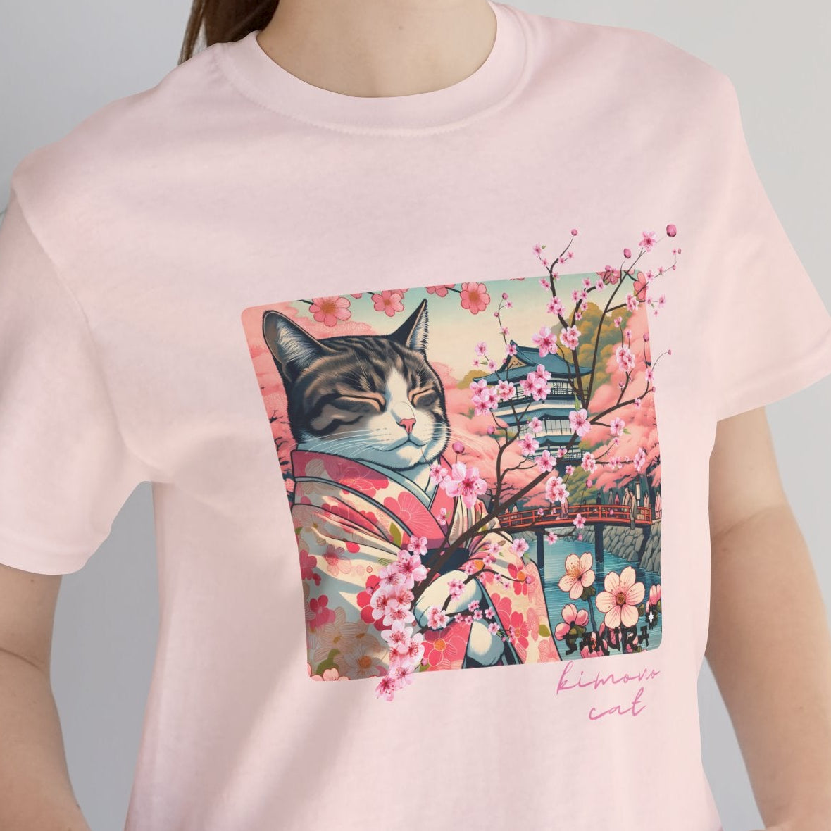 Person wearing a pink t-shirt with a cat graphic and cherry blossoms, standing indoors.