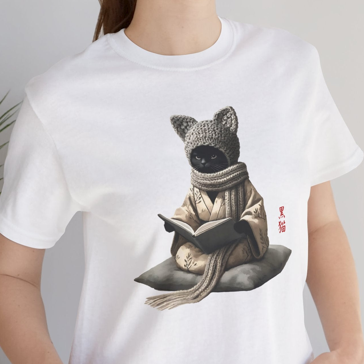 Person wearing a white t-shirt with a graphic of a bear in a sweater reading a book, standing indoors.