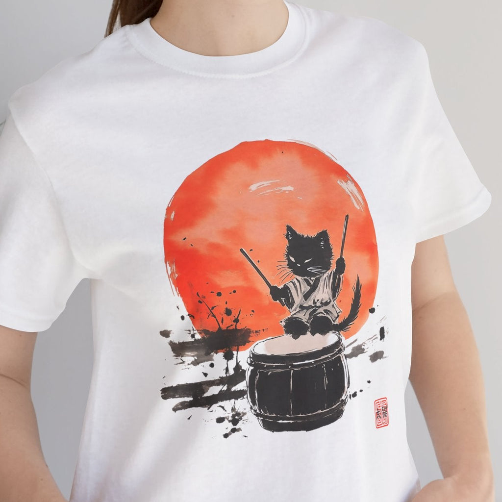Person wearing a white t-shirt with a graphic design of a cat playing drums against an orange sun, standing indoors.