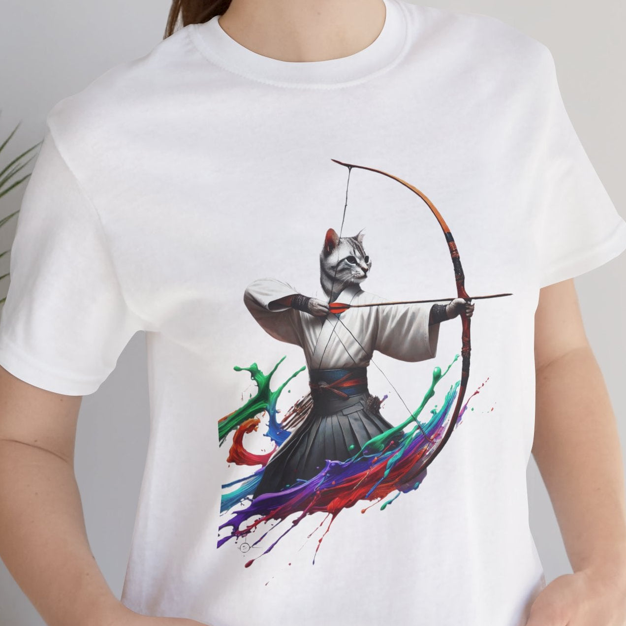 Person wearing a white t-shirt with a colorful graphic design, standing indoors next to a plant.